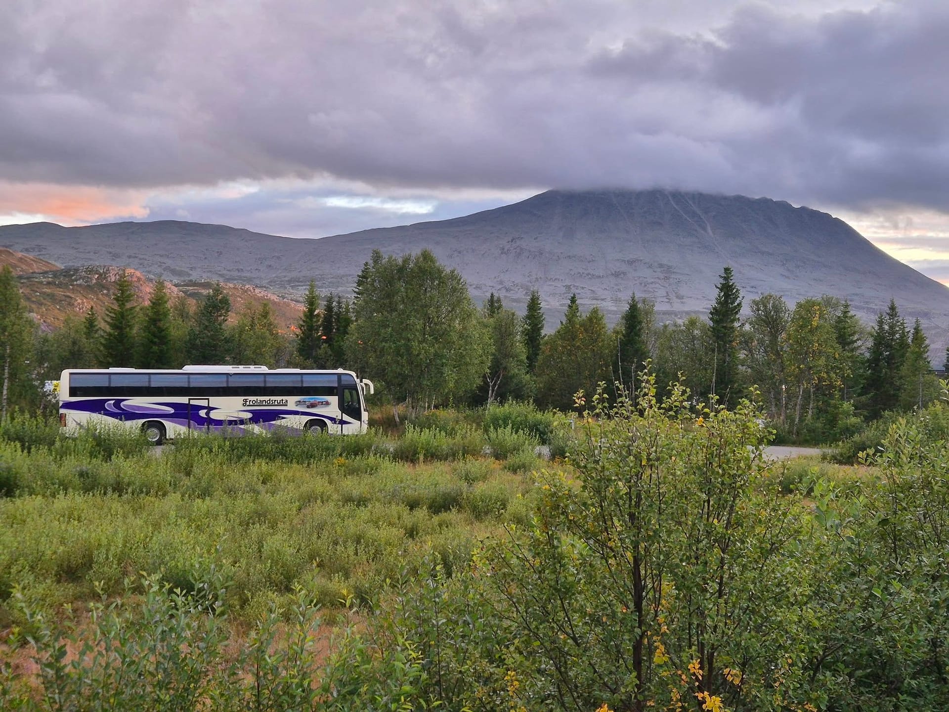 Frolandsruta-bussen parkert under et fjell i kveldslys